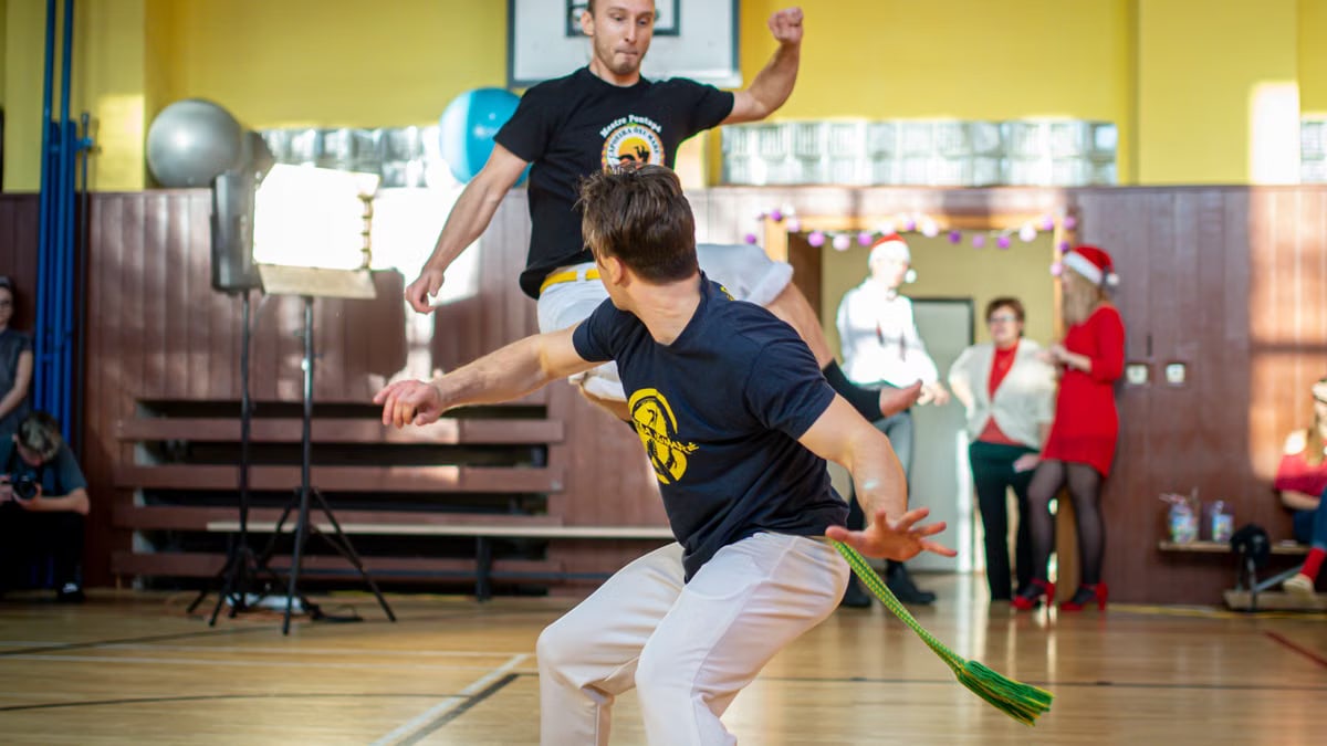 Energetic capoeira performance indoors with audience during daytime.